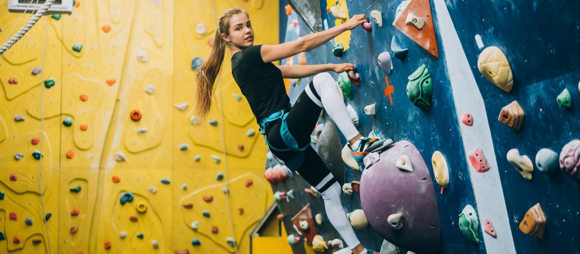 Young girl climbing a tall, indoor, man-made rock climbing wall